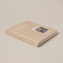 A hardcover book titled "The Space That Keeps You" by Jeremiah Brent lies on a beige surface. The cover, part of the Sunday Selects collection, is a soft beige hue and features a small black-and-white photograph of a chair and table on the front. 