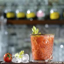 bloody mary with ice and tomato in front of a bar area 