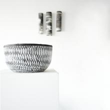 3 cylinders made by ceramic artist jodi walsh are on the wall behind a wood bowl that is ebony and white 