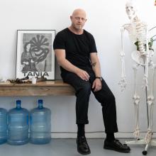 Pieter Hugo inside his studio sitting on a table next to a skeleton.  