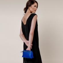 Back view of Model is wearing black dress and holding a blue purse behind her.  
