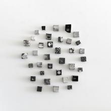 A photo showcasing a ceramic cube wall sculpture by Jodi Walsh, featuring various textured black and white blocks in a circular wall arrangement. 