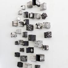 A photo showcasing a ceramic cube wall sculpture by Jodi Walsh, featuring various textured black and white blocks in a circular wall arrangement. 